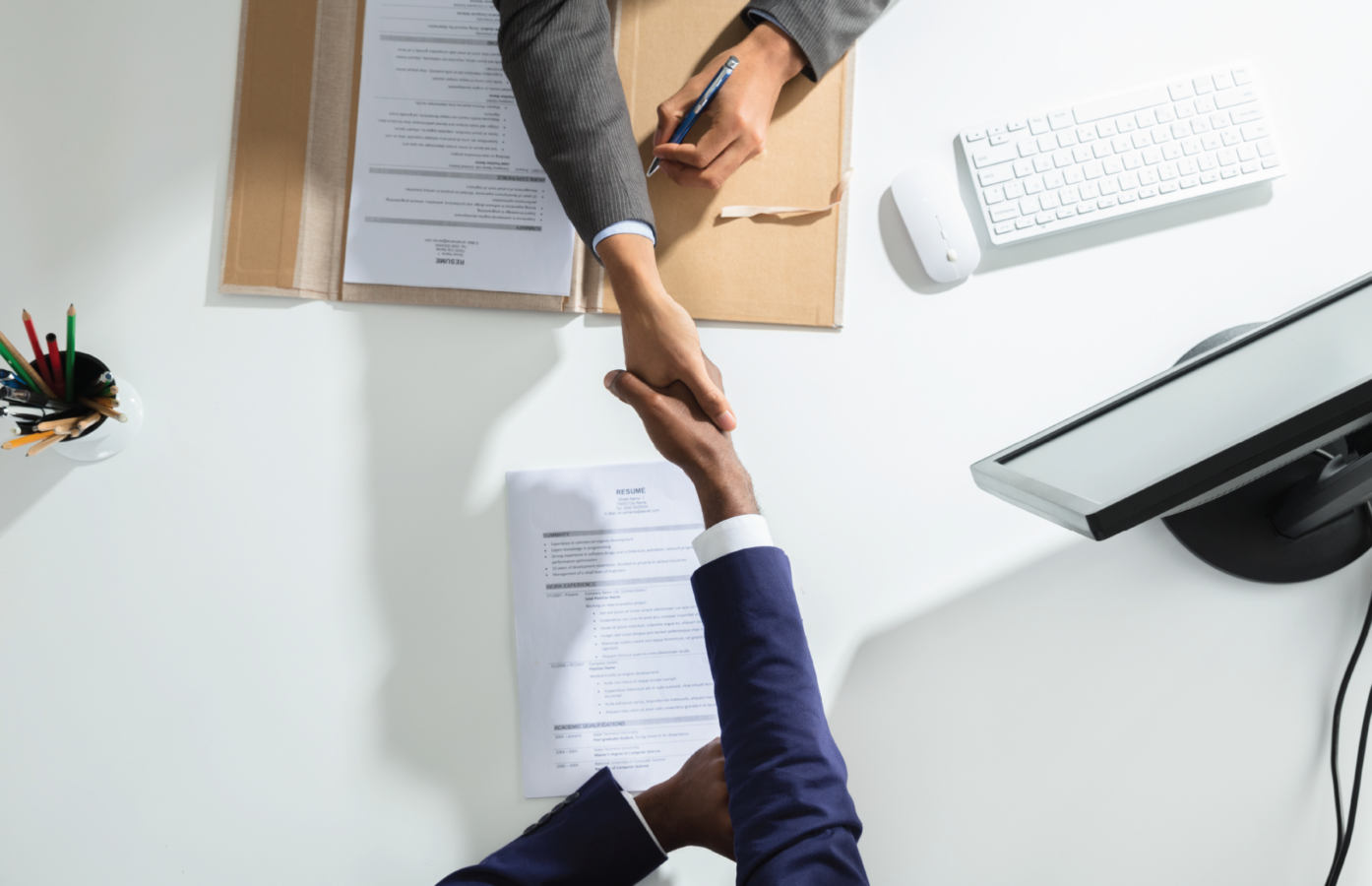 Two people shake hands over top of a desk