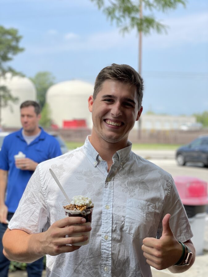 A man holds a thumbs up while smiling with ice cream