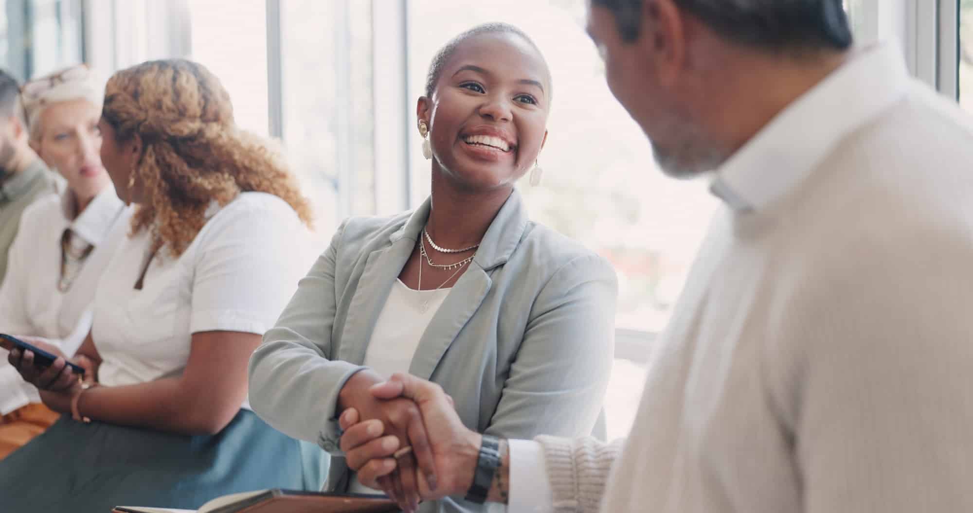 Handshake, hiring or people networking in waiting room before a recruitment job interview in an advertising agency. Partnership, relaxing or happy employees shaking hands, meeting or greeting in line.