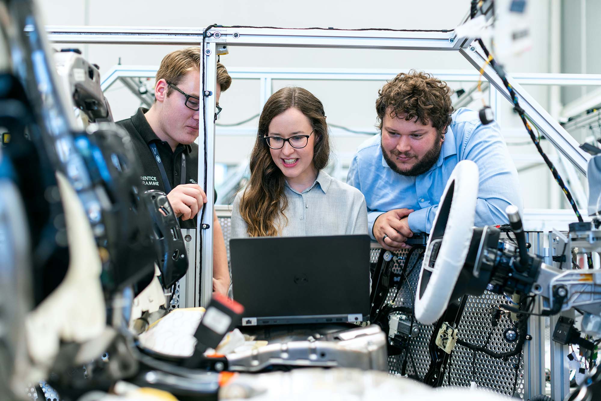 Three engineers collaborating around a laptop in a technical development workspace