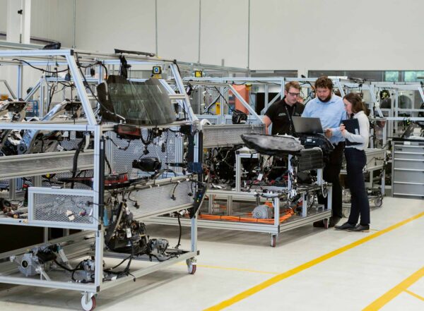 Engineers reviewing automotive components on a laptop at a mobile workstation in a manufacturing lab