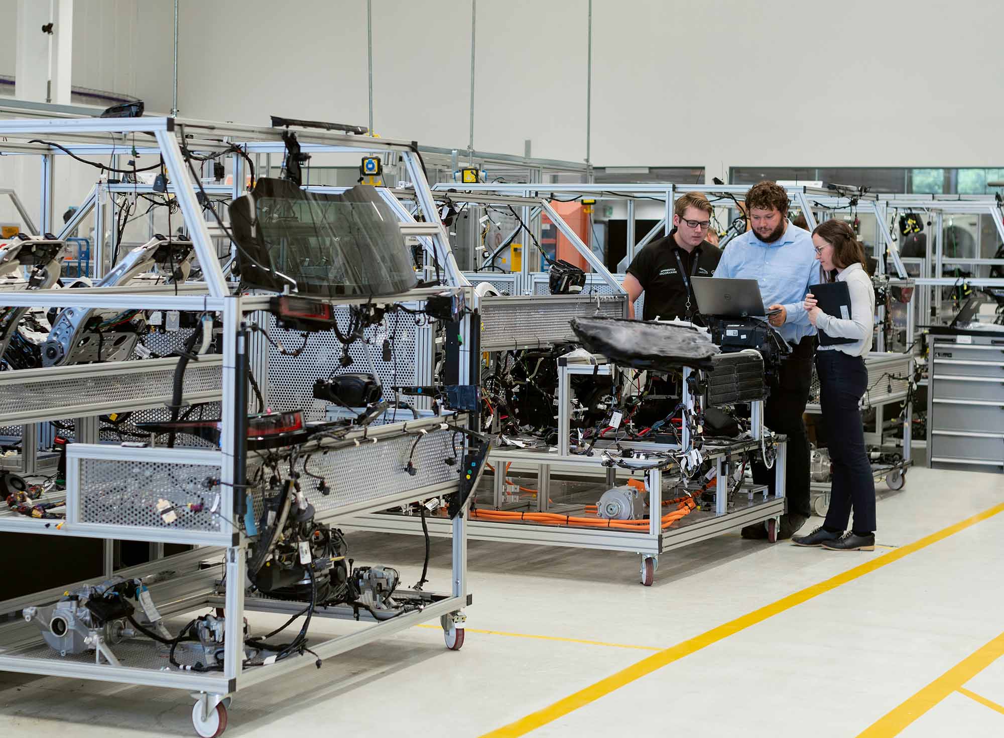 Engineers reviewing automotive components on a laptop at a mobile workstation in a manufacturing lab
