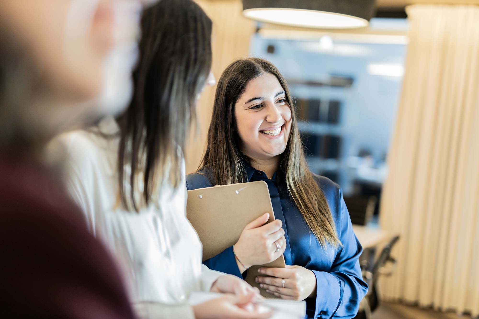Smiling professional holding a clipboard while talking with colleagues in a bright office