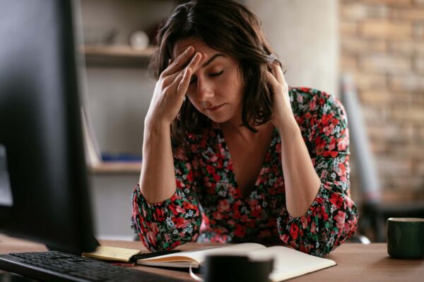 Recruiter at a desk with eyes closed and hand on forehead, looking stressed beside a computer and notebook