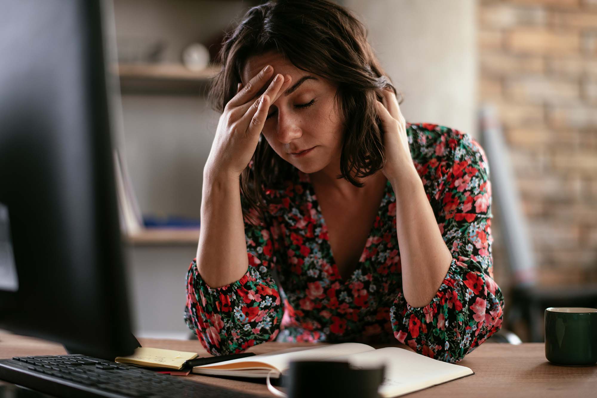 Recruiter at a desk with eyes closed and hand on forehead, looking stressed beside a computer and notebook