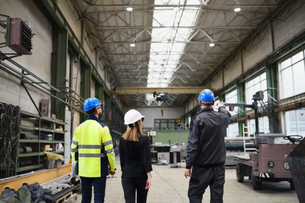 Three colleagues in hard hats walking through a manufacturing plant during a facility walkthrough