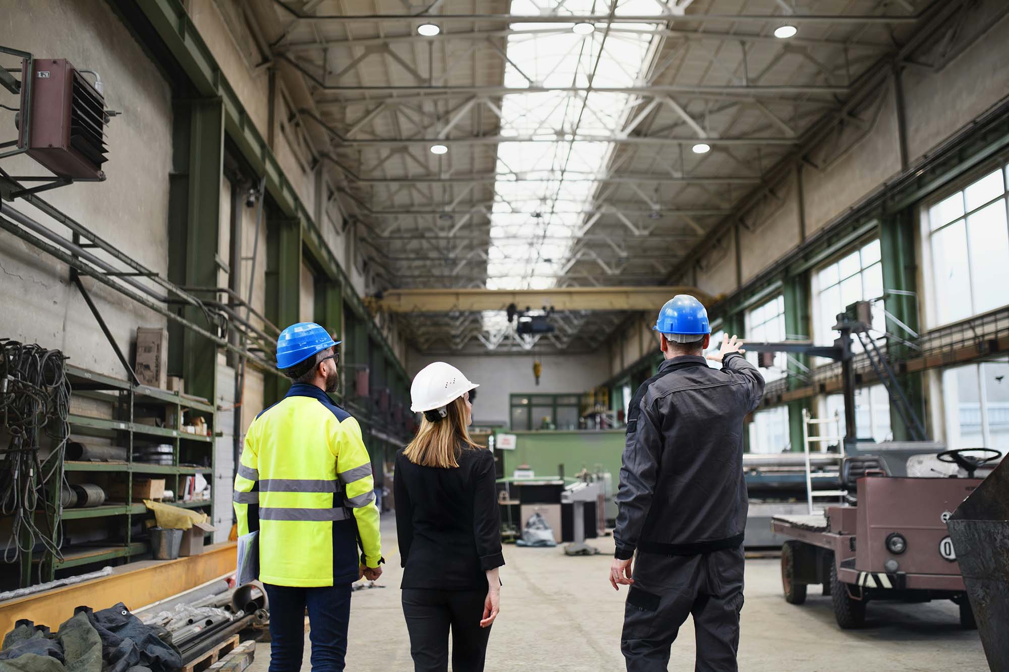 Three colleagues in hard hats walking through a manufacturing plant during a facility walkthrough