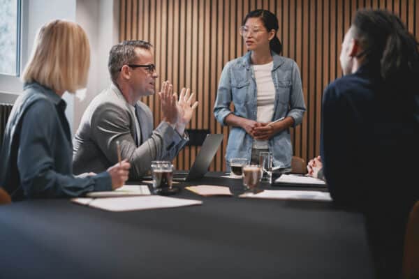 Colleagues discussing work around a conference table in a meeting room
